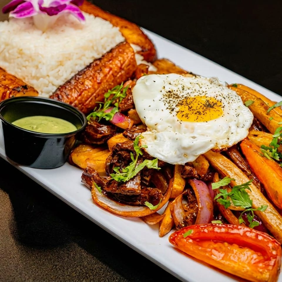 Peruvian Lomo Saltado with rice, fried plantains, sunny-side-up egg, and green sauce.