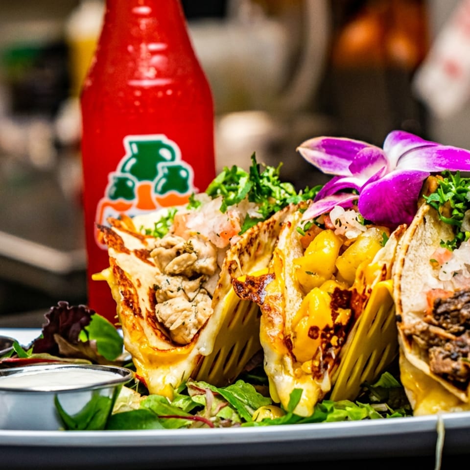 Plate of three loaded tacos with diverse fillings, sauces, and a red soda bottle.