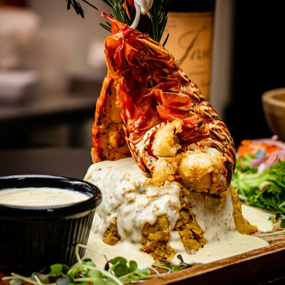 Grilled split lobster tail over creamy rice, with a side salad and dipping sauce on a wooden board.